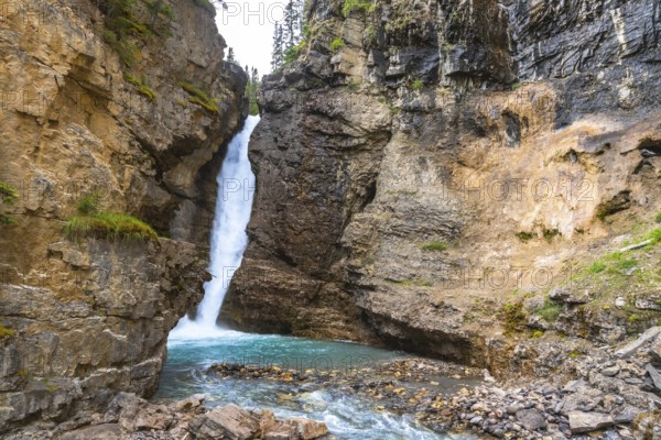 Cascading waterfall flowing into a vibrant turquoise pool in johnston canyon, surrounded by rugged