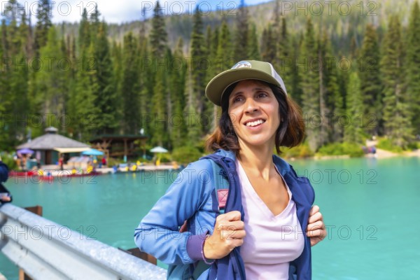 Female hiker wearing a baseball cap and backpack standing near the turquoise waters of emerald