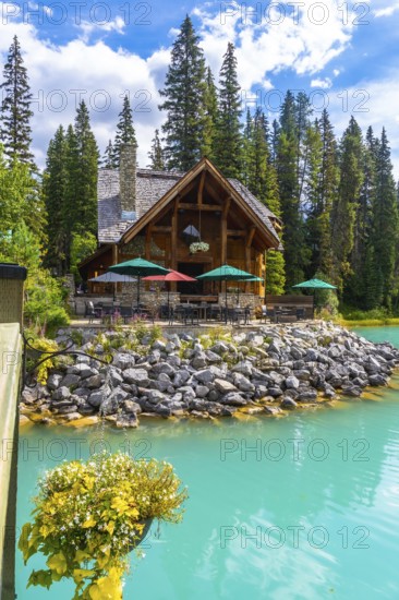 Wooden lodge with patio furniture and umbrellas reflecting in turquoise water on the shore of