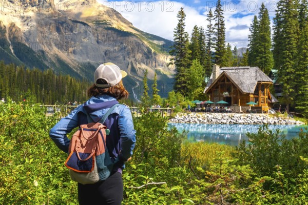 Tourist with a backpack is enjoying the breathtaking view of emerald lake and its charming wooden