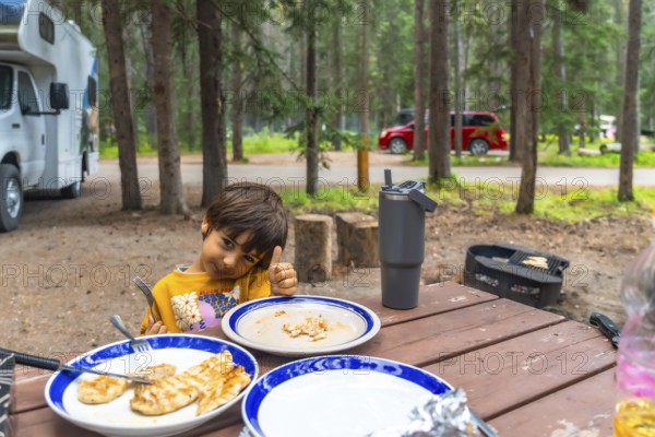 Young camper giving a thumbs up after enjoying a delicious barbecue meal at a campsite in banff