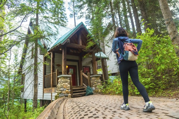 Female tourist with backpack walking on a paved path. Admiring a wooden cabin in the forest near