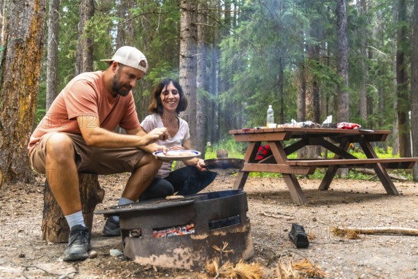 Tourists enjoying the warmth of a campfire while cooking delicious meals during their camping