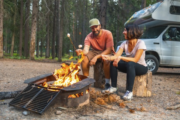 Tourists are roasting marshmallows over a campfire near their campervan in a campsite in banff