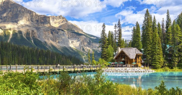 Wooden lodge sitting on the shore of a turquoise lake reflecting in the calm water with tourists