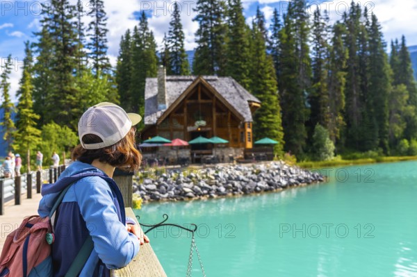 Female hiker admiring the turquoise waters of emerald lake and its charming lodge, nestled among