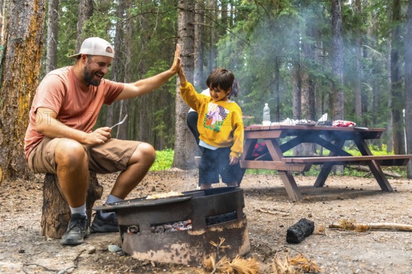 Father and son are giving a high five while grilling food over a campfire, enjoying quality time