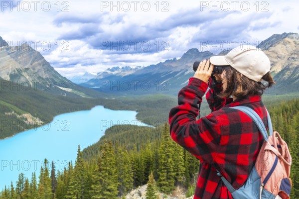 Female hiker using binoculars admires the stunning turquoise waters of peyto lake and majestic