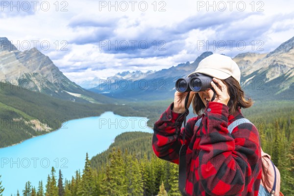 Female hiker using binoculars, admiring the scenic turquoise waters of peyto lake and the majestic