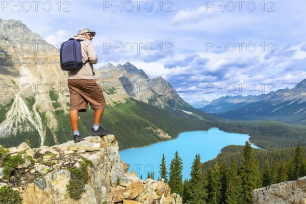 Photographer standing on a rocky cliff captures a breathtaking view of turquoise peyto lake