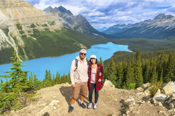 Two hikers are standing on a mountaintop, enjoying the breathtaking panoramic view of the turquoise