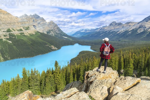 Female hiker standing on a rocky cliff enjoying breathtaking view of turquoise peyto lake and