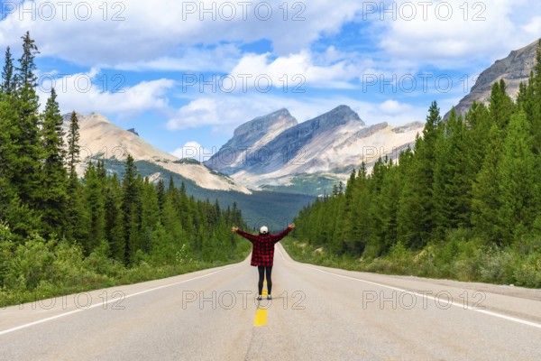 Female tourist standing on a scenic road with open arms, enjoying the freedom and breathtaking view