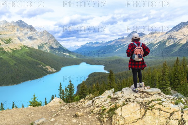 Female hiker standing on a rocky cliff, gazing at the turquoise waters of peyto lake and the