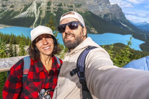 Two happy tourists are taking a selfie with peyto lake and the canadian rockies in the background