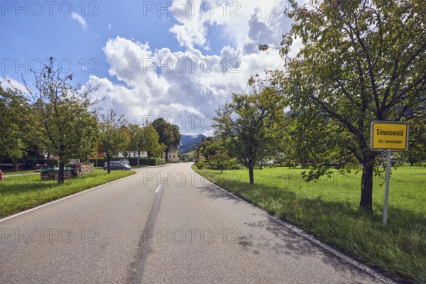 Landscape, town entrance sign, road, houses, trees with autumn leaves, hills, coniferous forest,