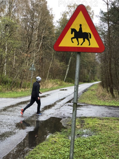 Person jogging on wet forest road with road sign for riding on horse in Ystad, Skåne County,