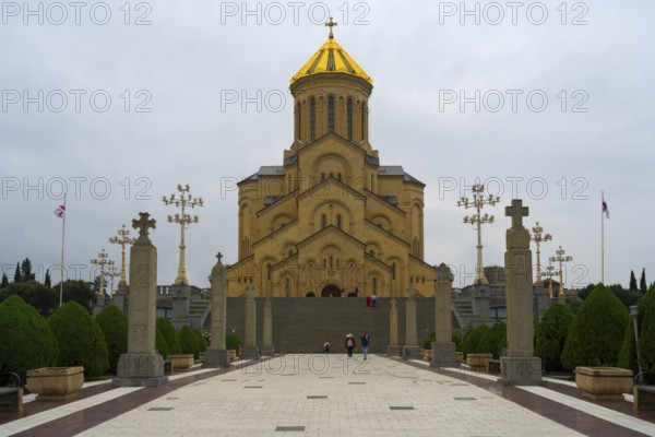 Grand cathedral with golden roof and stylish stone pillars against cloudy sky, Sameba Cathedral,