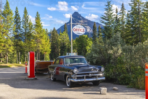 Vintage car towing a wooden boat trailer parked near a vintage gas pump by the johnston canyon