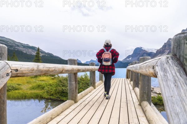 Female tourist walking on a wooden bridge enjoying the breathtaking view of bow lake and