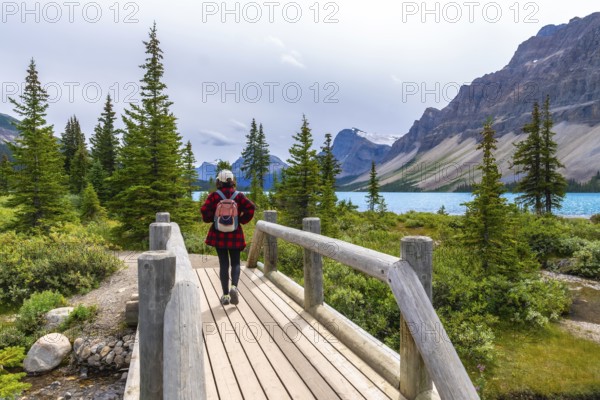 Female tourist walking on a wooden bridge and enjoying the breathtaking view of bow lake and