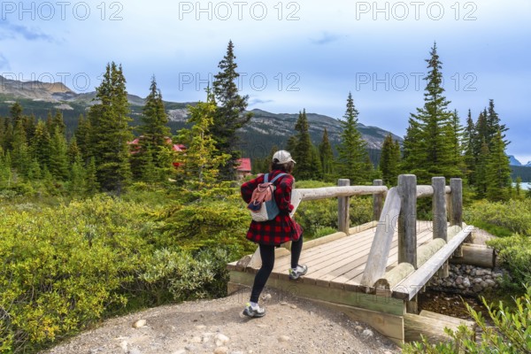 Female tourist walking across a wooden bridge at bow lake, framed by a red roofed building,