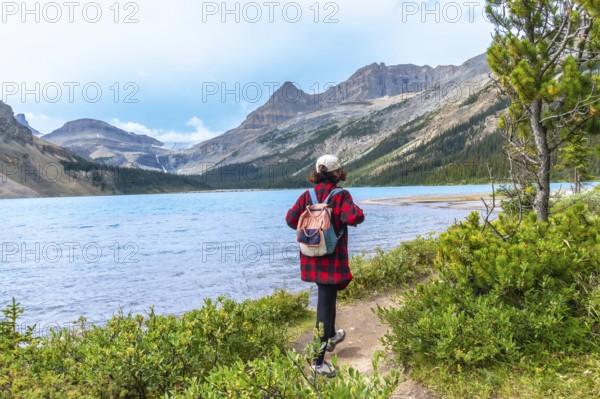 Female tourist with backpack walking along hiking trail by turquoise bow lake with crowfoot glacier