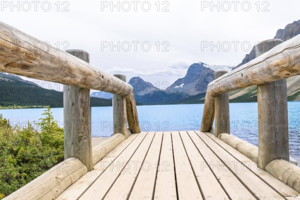 Wooden bridge leading to turquoise waters of bow lake, framed by the majestic canadian rockies in
