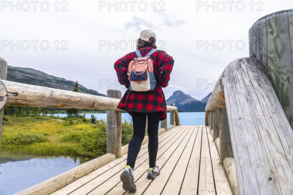 Female tourist walking on wooden bridge enjoying the scenic view of bow lake and surrounding