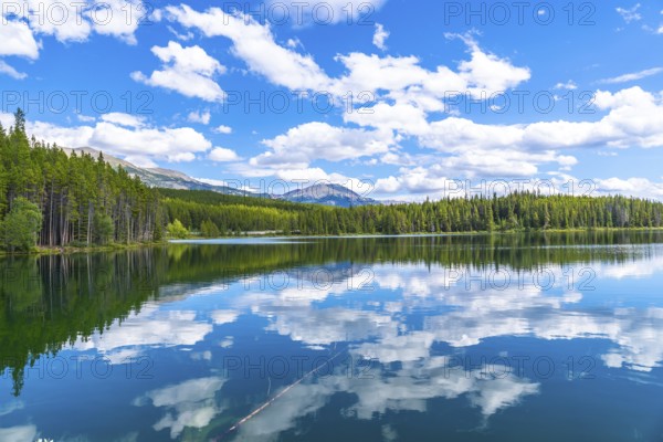 Calm waters reflecting a stunning cloudy sky over herbert lake, surrounded by lush pine forests and