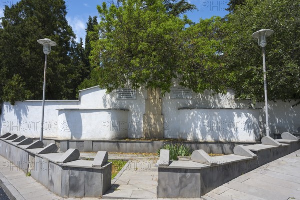 Small park with memorial and trees, surrounded by a white wall, modern lanterns illuminate the