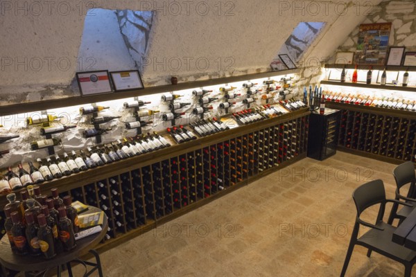 Wine cellar with illuminated shelves full of wine bottles and simple chairs and tables for