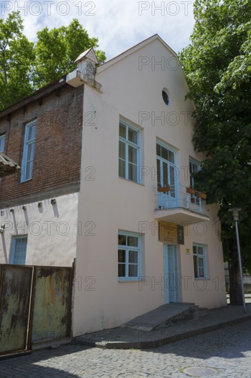 Two-storey building with bricks and blue door, surrounded by trees on a sunny day, Katharinenfeld
