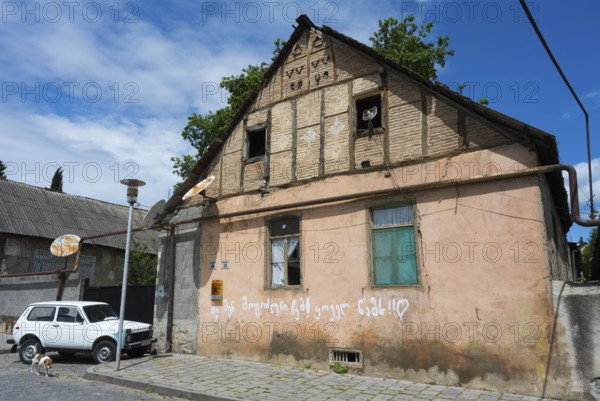 A dilapidated house with leaning antennas and graffiti, next to a parked car under cloudy sky,