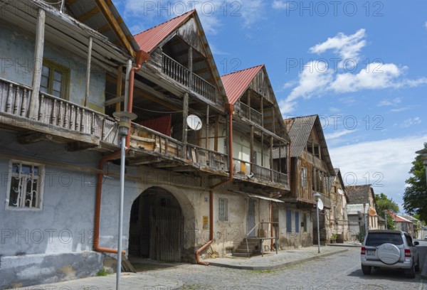 Street view with old wooden houses and balconies under blue sky with parked cars, traditional