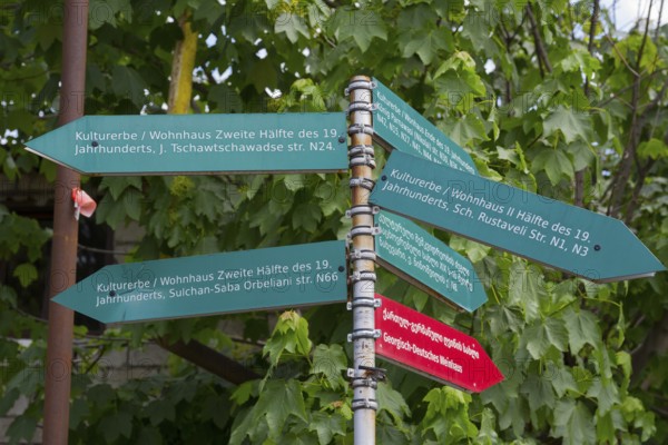 Green signpost with signs showing the cultural heritage of the 19th century under trees, Bolnissi,
