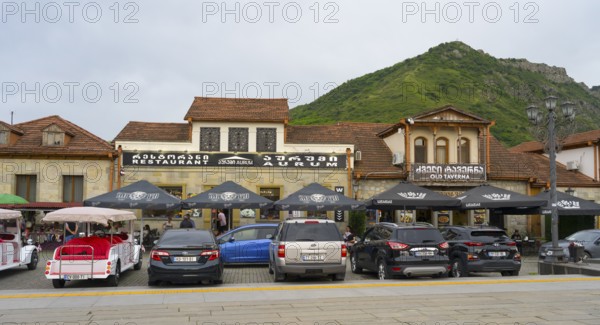 Street scene with cars parked in front of a restaurant with mountain backdrop in the background,
