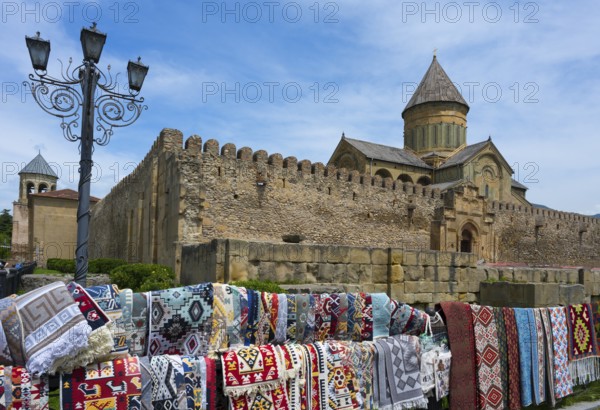 Rugs in front of a historic wall with a cathedral in the background under a blue sky,
