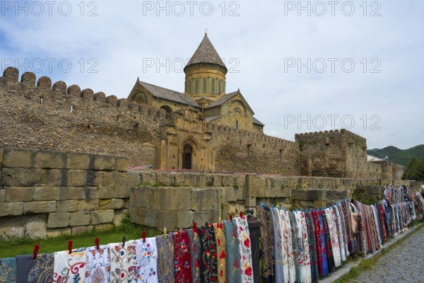 Stone fortress with monastery in the background, lots of colorful fabrics hung in front of it,