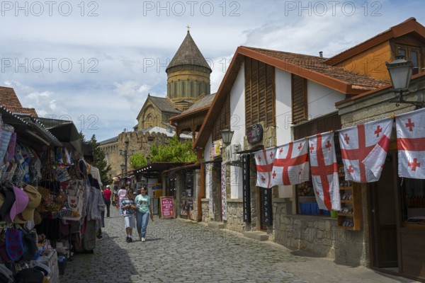 Street with souvenir stands, Georgian flags and a church in the background, Svetitskhoveli