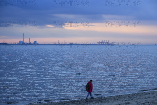 Person on the beach with a view of the sea and industrial areas in Wilhelmshafen right Jade-Weser