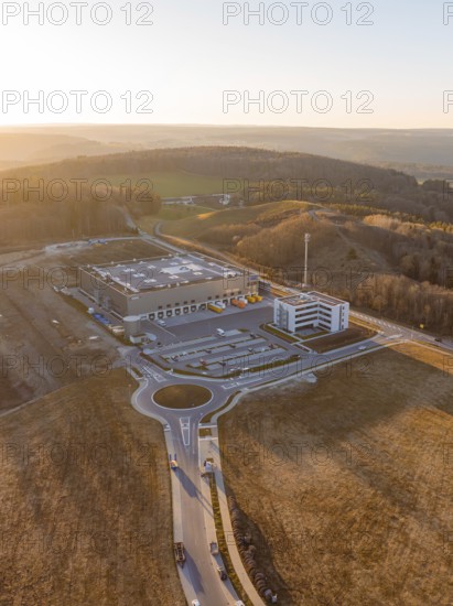 Industrial complex with circular road next to hilly landscape at sunset, future PV construction on