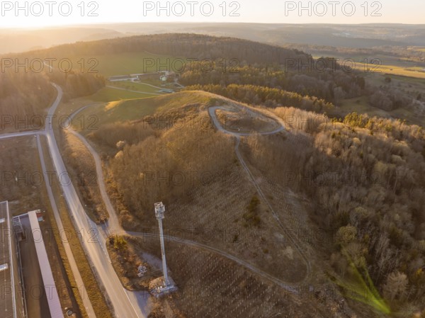 Hilly landscape with forest and roads in the warm light of sunset, future PV building on old