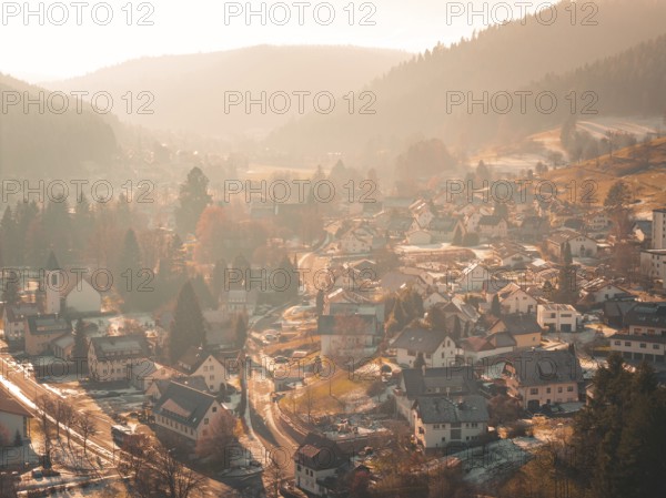 A picturesque village is situated in a valley surrounded by hilly forests and gentle autumn fog,
