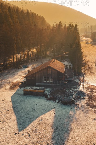 Wooden house on the edge of a forest whose shadows are cast in the snow by warm sunset light,