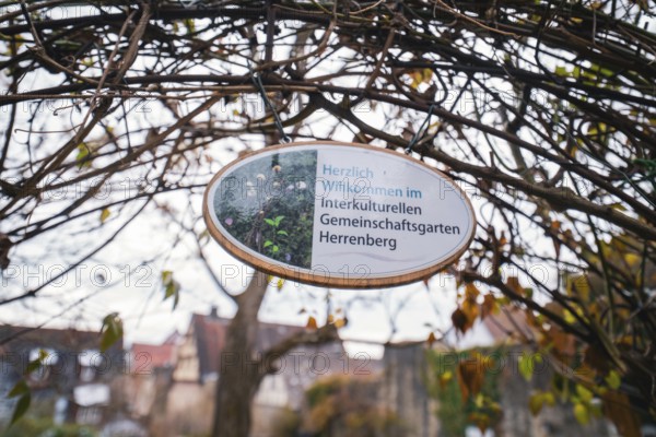 Wooden sign with welcome text for the intercultural community garden surrounded by branches,