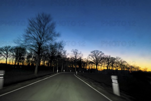 View from speeding speeding car at dusk at nightfall on a country road illuminated by headlights