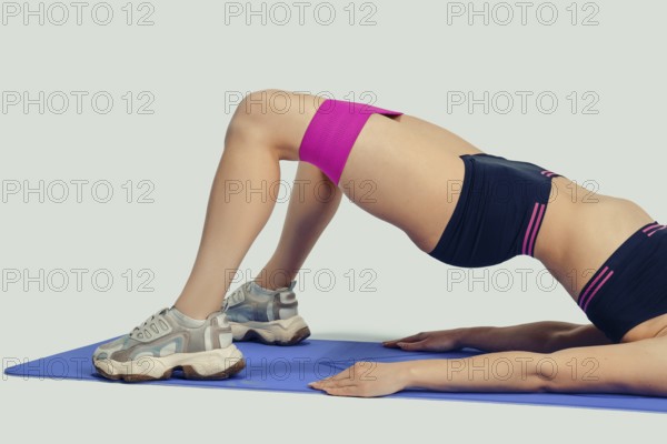 Unrecognizable woman lies on her back on a blue exercise mat, lifting her hips while using a