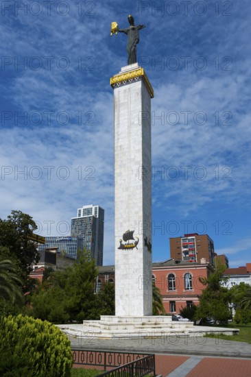 High column with statue in front of modern buildings under clear sky, statue of Medea, Europe