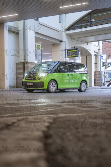 Green shuttle goes around a bend in an urban area, busy atmosphere, Deer E-Mobility Shuttle